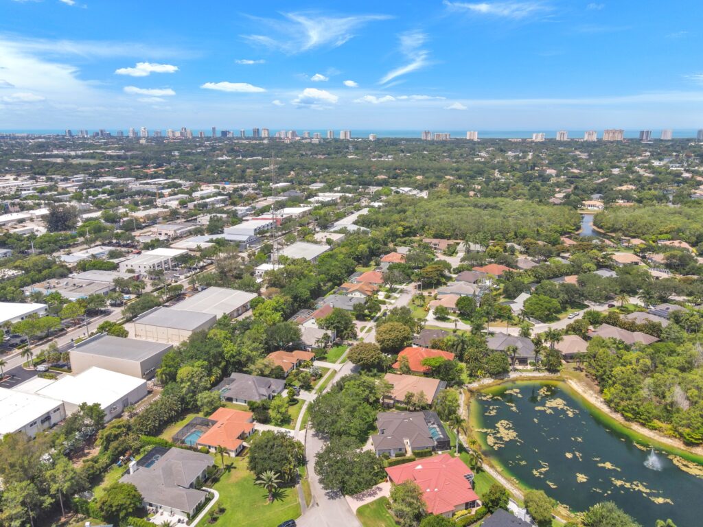 Aerial drone photo of a North Naples, FL neighborhood with a lake and the Gulf coast skyline beyond